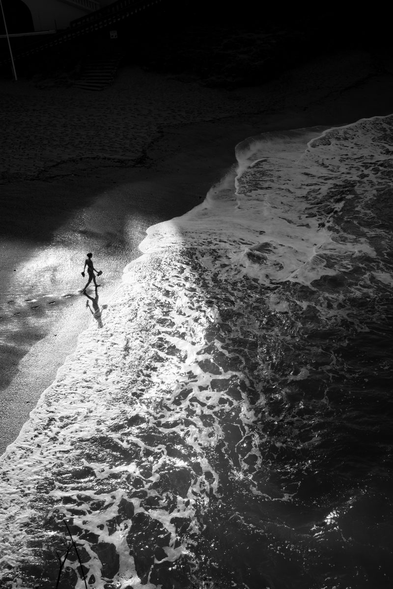 Black and white view from above of a lone figure walking along the surf line, Biarritz france