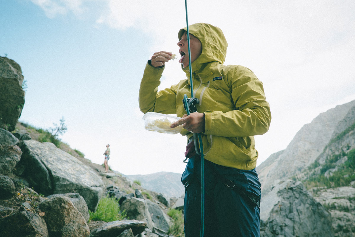 A belayer in a yellow jacket eating a snack while belaying