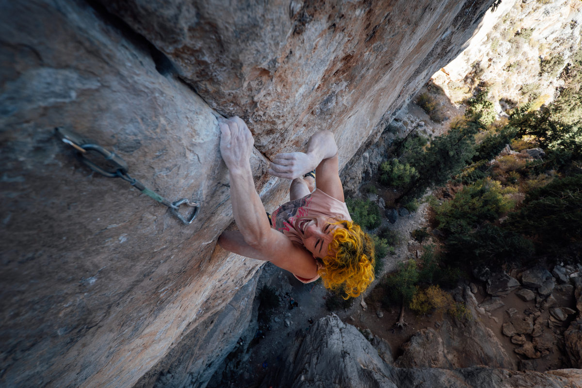 Looking straight down on a climber pulling hard on a steep limestone wall, the ground far below