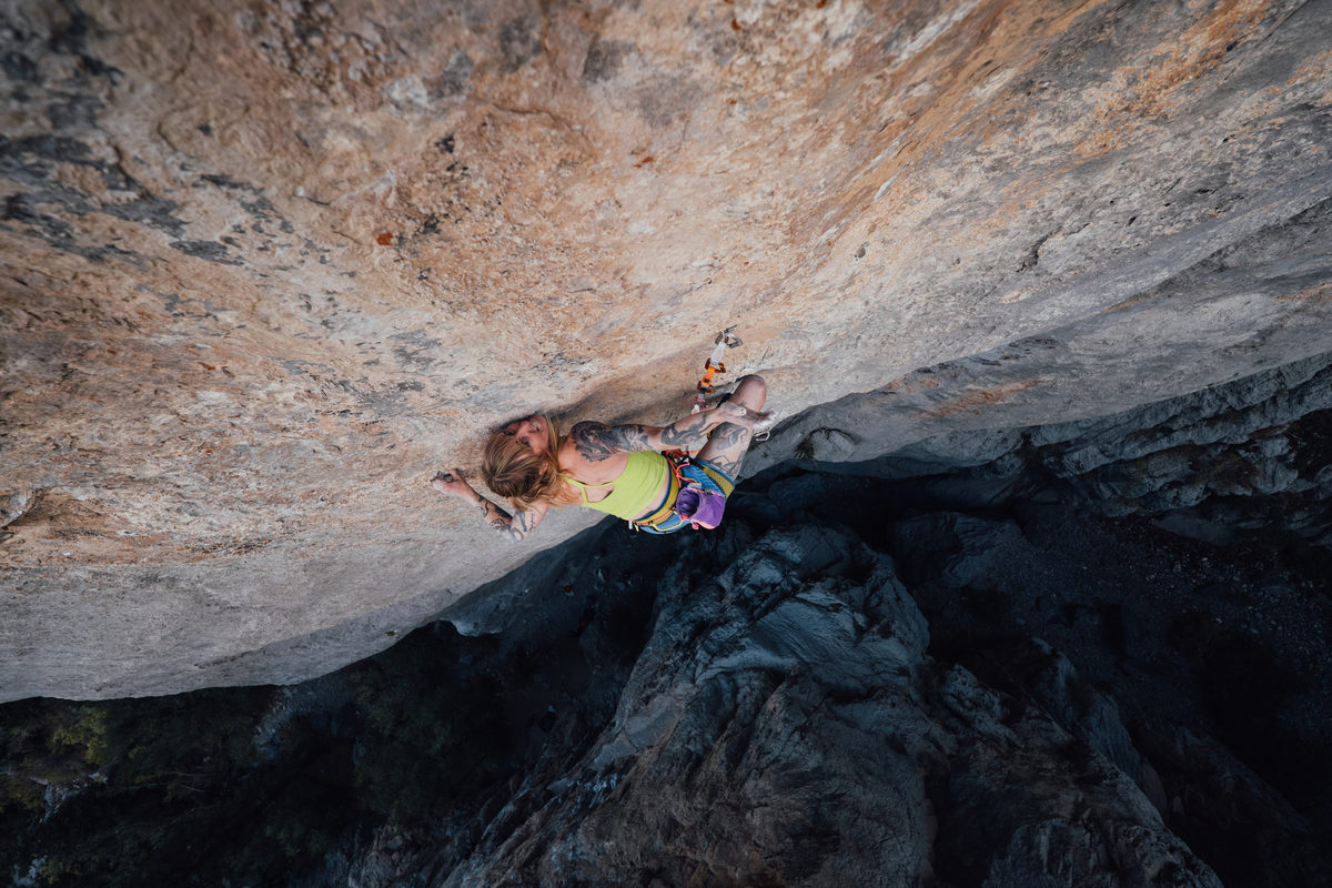 A climber stretched out beneath a wide overhanging roof above a rocky landing