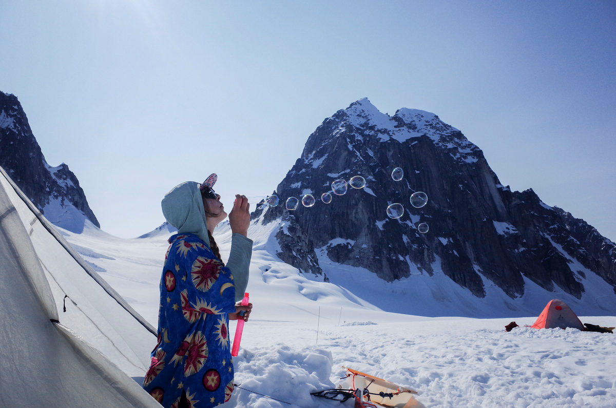A figure in a patterned jacket blowing bubbles on a glacier