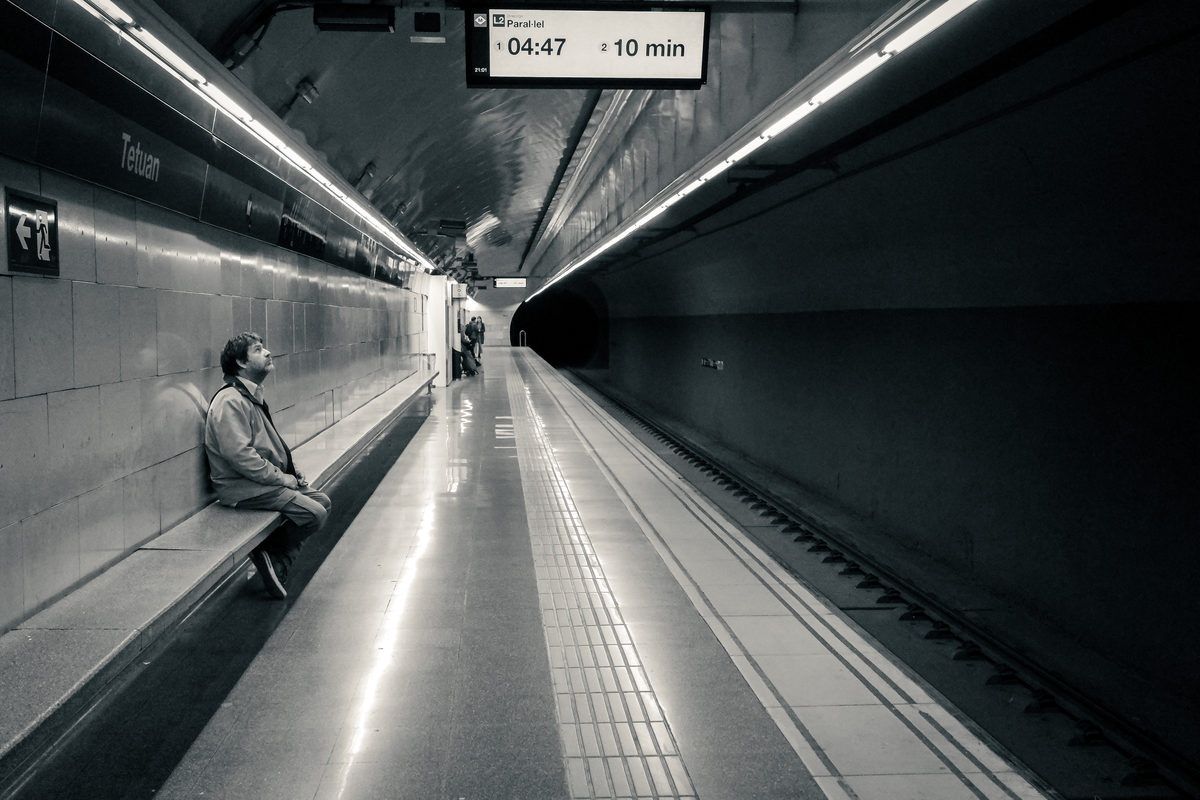 Black and white: a lone figure waiting on a bench in a long underground tunnel
