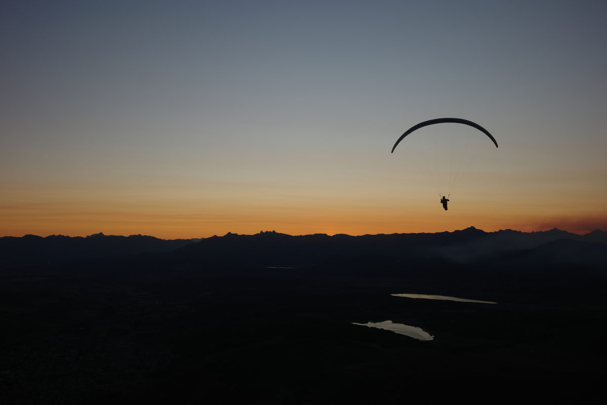 A paraglider silhouetted against an orange sky above dark ridgelines at dusk