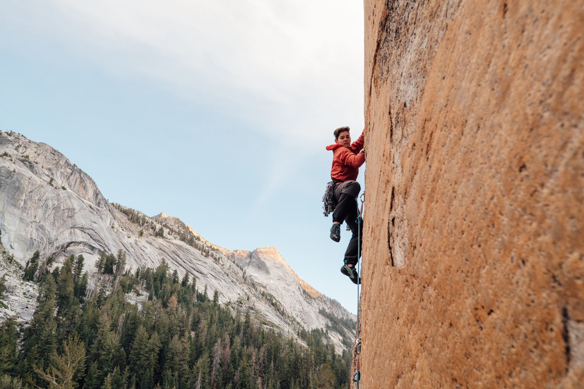 A climber in a red jacket on an orange granite wall. Carlin Reynolds climbing