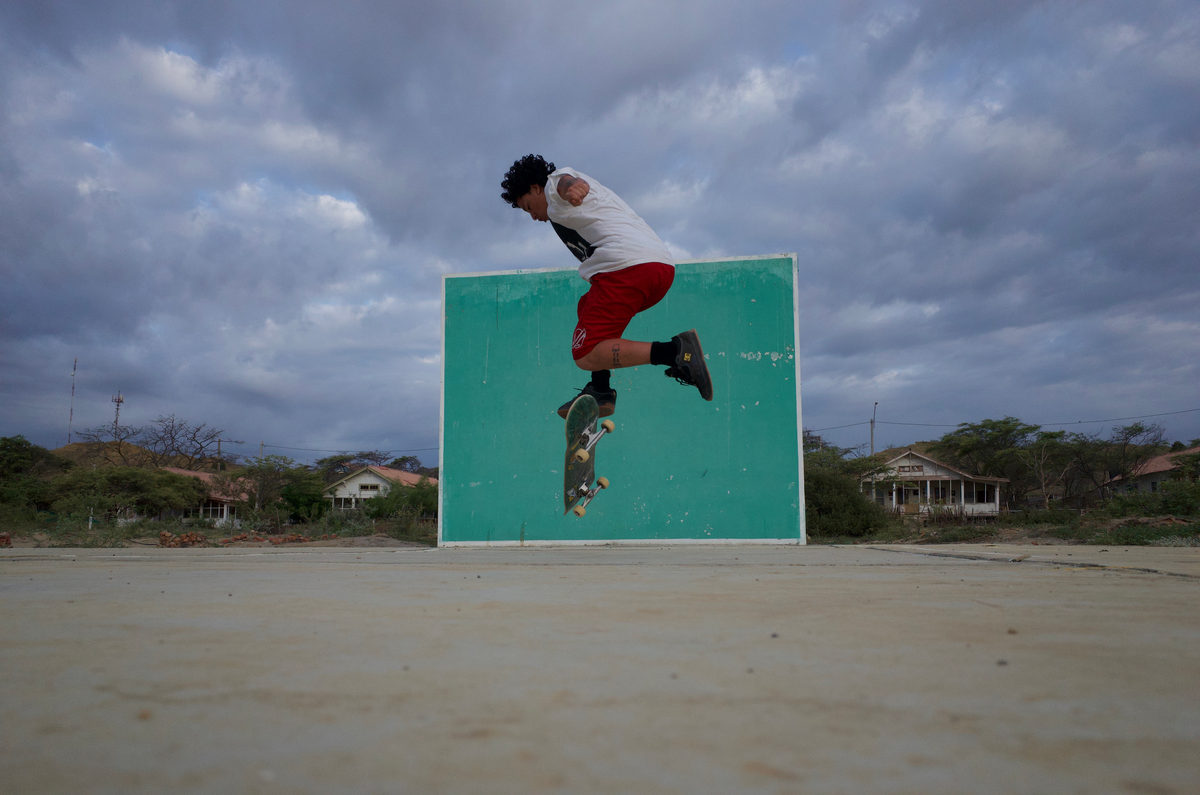 A skateboarder doing a trick in front of a green wall in Lobitos, Peru.